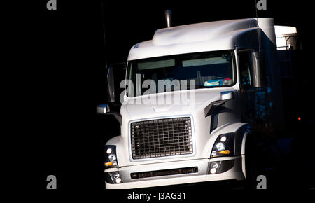 Große leistungsstarke weiße bonneted rig Semi Truck von der Sonne beschienen bewegt sich mit der kommerziellen Ladung zum Licht von dichtem schwarzen Schatten, Erstellen der e Stockfoto