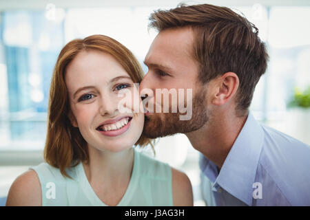 Liebevoller Mann küsst Frau im Büro Stockfoto
