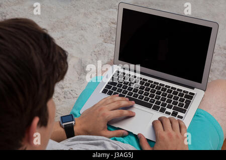 Erhöhte Ansicht von Mann mit Laptop sitzend auf Stuhl am Strand Stockfoto