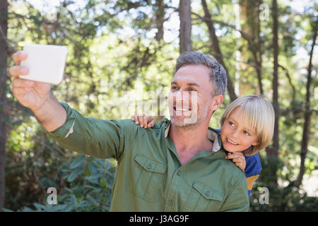 Lächelnd, Vater und Sohn nehmen Selfie mit Mobile im Wald Stockfoto