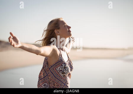 Glückliche Frau mit ausgestreckten Armen an sonnigen Tag am Strand stehend Stockfoto