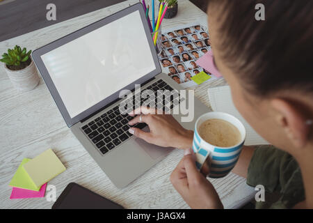 Vogelperspektive Blick auf weibliche Bildbearbeitungsprogramm halten Kaffeetasse während mit Laptop im Büro Stockfoto