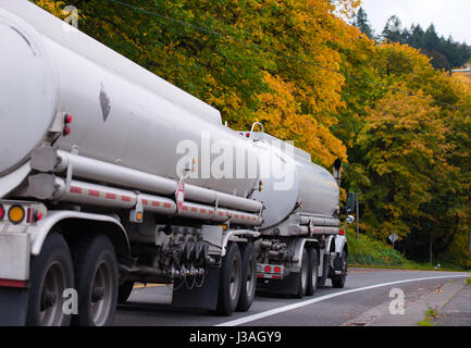 Moderne Big Rig Semi Truck ziehen zwei weißen Tank Anhänger mit brennbaren Materialien entlang einer malerischen kurvenreiche Straße mit Herbst vergilben Bäume Stockfoto