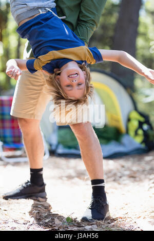 Verspielte Vater Holding Sohn kopfüber auf Campingplatz Stockfoto