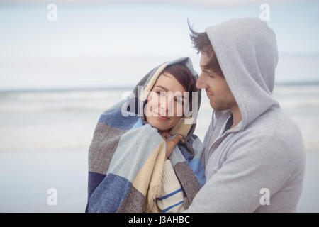 Junger Mann umarmte ihre Freundin gewickelt in Decke am Strand im winter Stockfoto