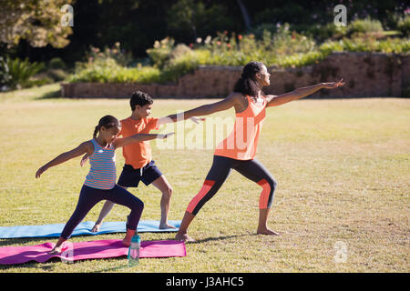 Junge weibliche Trainer mit Kindern üben Virabhadrasana II stellen im park Stockfoto