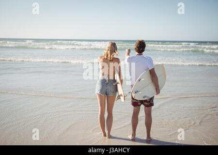 Rückansicht des Paares hält Surfbretter stehen am Strand im sonnigen Tag Stockfoto