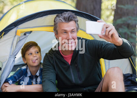 Verspielte Vater und Sohn Grimassen während der Einnahme von Selfie im Zelt Stockfoto