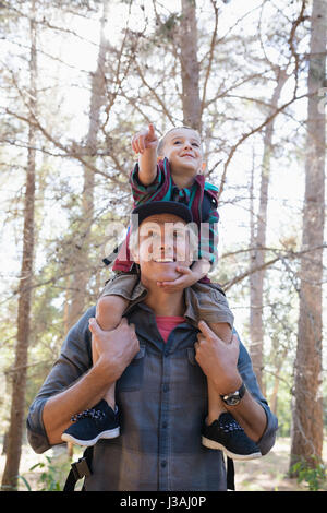 Niedrigen Winkel Blick auf Vater mit Sohn auf Schultern und zeigt im Wald Stockfoto