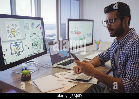 Junger Geschäftsmann mit Handy während der Arbeit am Schreibtisch im Büro Stockfoto