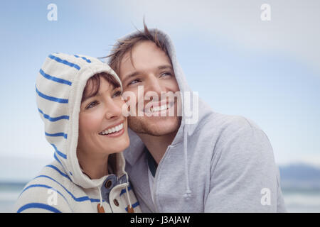 Lächeln, paar tragen Kapuzen Pullover während der Suche entfernt am Strand im winter Stockfoto