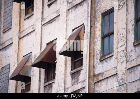 Die Äußere Mauer des alten funktionsunfähig heruntergekommenen verlassenen mehrstöckige Industriebau aus bemalten Ziegeln mit Reihen von Fenstern und rostiges Metall Stockfoto