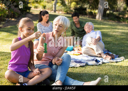 Großmutter ihre Enkelin bläst Seifenblasen im Park an einem sonnigen Tag zu betrachten Stockfoto