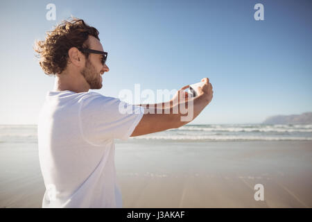 Glücklicher Mann nehmen Selfie gegen blauen Himmel am Strand während der sonnigen Tag Stockfoto