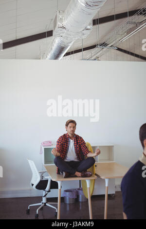 Junger Geschäftsmann Yoga beim Sitzen am Schreibtisch im Büro zu tun Stockfoto