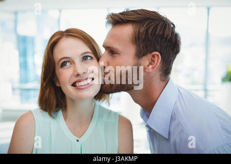 Liebevoller Mann küsst Frau im Büro Stockfoto