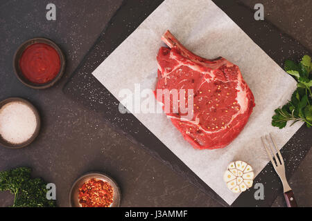 Rohes Frischfleisch Rib-Eye Steak und Gewürze auf schwarzem Stein Schiefer Hintergrund. Draufsicht, Leerzeichen, Vintage getönten Bild Stockfoto