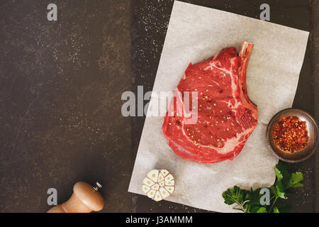 Rohes Frischfleisch Rib-Eye Steak und Gewürze auf schwarzem Stein Schiefer Hintergrund. Draufsicht, Leerzeichen, Vintage getönten Bild Stockfoto