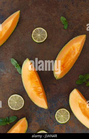 Scheiben Melone Melone und Kalk auf rustikalen dunklen Hintergrund. Ansicht von oben, Raum zu kopieren, flach zu legen Stockfoto