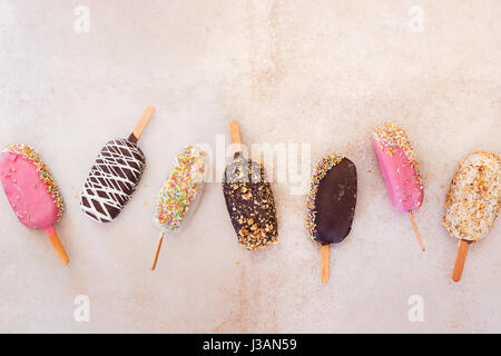 Eis-sticks mit Schokolade, Obst, gerösteten Mandeln und bunten Zucker Streusel auf rustikalen Hintergrund. Ansicht von oben, Leerzeichen Stockfoto