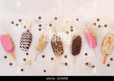 Eis-sticks mit Schokolade, Obst, gerösteten Mandeln und bunten Zucker Streusel auf rustikalen Hintergrund. Ansicht von oben, Leerzeichen Stockfoto