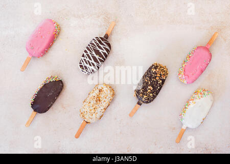 Eis-sticks mit Schokolade, Obst, gerösteten Mandeln und bunten Zucker Streusel auf rustikalen Hintergrund. Ansicht von oben, Leerzeichen Stockfoto