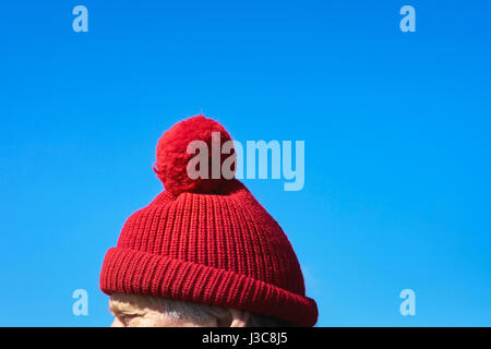 Alter Mann mit einem roten bobble Cap (Pudelmütze) bei kaltem Wetter mit strahlend blauem Himmel auf der kleinen Nordfriesland-Insel Amrum, Deutschland Stockfoto