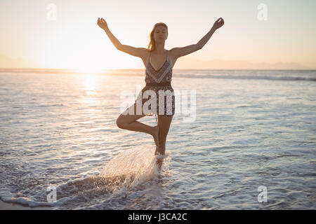 Frau tut Yoga im Meer am Strand während der Dämmerung Stockfoto