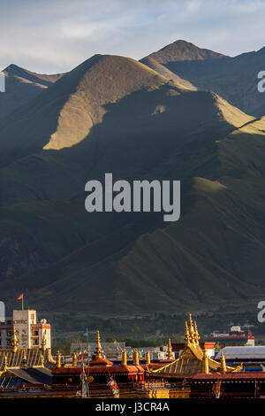 Goldenen Zinnen des Jokhang Tempels unter vielen Dächern der Häuser in Lhasa Stadt und späten Nachmittag Sonnenlicht auf Berg im Hintergrund Stockfoto