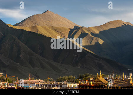 Goldenen Zinnen des Jokhang Tempels unter vielen Dächern der Häuser in Lhasa Stadt und späten Nachmittag Sonnenlicht auf Berg im Hintergrund Stockfoto