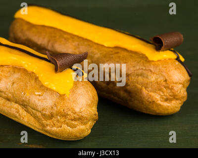 Zwei Choux Pastry Orange Eclairs gegen eine grüne Backgroound Stockfoto