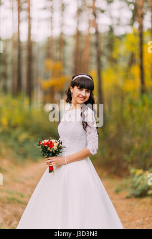Schöne unschuldige junge Brünette Braut im klassischen weißen Kleid steht auf Waldweg Stockfoto