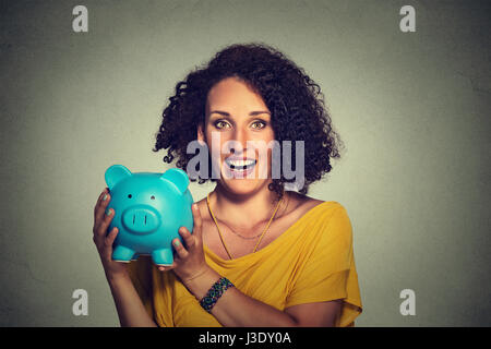 Closeup Portrait glücklich, Lächeln, Geschäftsfrau, bank Mitarbeiter halten Sparschwein auf graue Wand Hintergrund isoliert. Finanzielle Einsparungen, Banking-Konzept Stockfoto