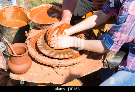 Potters Hände leiten ein Kind übergibt ihm helfen, mit den keramischen Rad arbeiten. Arbeiten Sie an der Töpferscheibe an die Natur Stockfoto