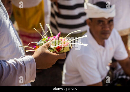 Bunte religiöse Angebote genannt Canang Sari von einer hinduistischen Anhänger an einer religiösen Zeremonie auf Bali in einer Hand getragen werden. Zuschauer im Hintergrund Stockfoto