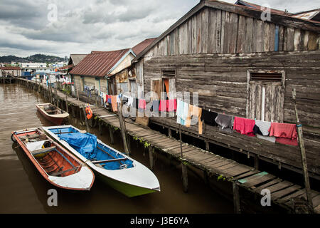 Pfahlbauten und Hütten in einem schwimmenden Dorf Szene mit Wäschereien Trocknung auf eine Wäscheleine und kleine Boote vor Anker neben einer Promenade auf Borneo river Stockfoto