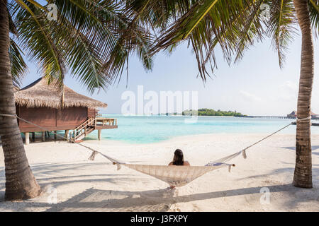 Exotische Tropenparadies Blick über Wasser Bungalow sitzen in Hängematte Crystal Clear Blau Türkis Meer Wasser Stockfoto