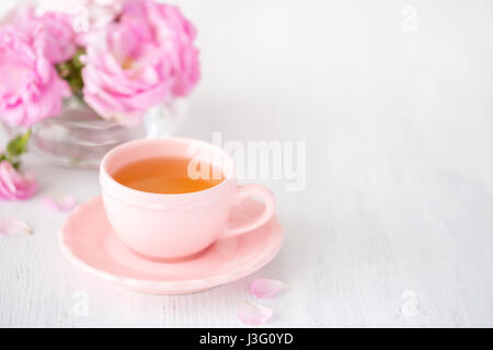 Tasse Tee und Strauß l rosa Rosen auf rustikalen Tisch. Stockfoto