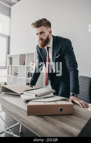 junger Geschäftsmann mit Dokumenten und Ordnern stehen am Tisch im Büro Stockfoto