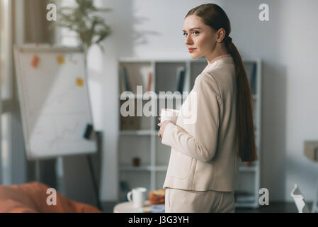 Seitenansicht der attraktive junge Geschäftsfrau holding Schale und wegschauen im Büro Stockfoto