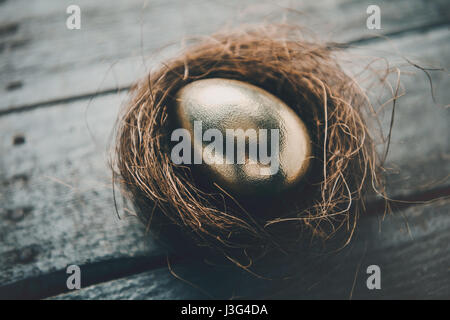 Vergrößerte Ansicht des goldenen Osterei im Nest auf Holztisch, Frohe Ostern-Konzept Stockfoto