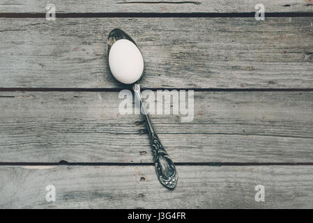 Draufsicht der weißen Hühnerei in silbernen Löffel auf hölzernen Tischplatte. Happy Easter-Konzept Stockfoto