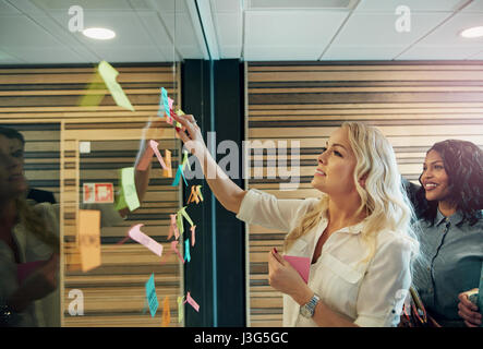 Die Geschäftsleute stehen an der Wand mit den Aufklebern und sprechen. Stockfoto