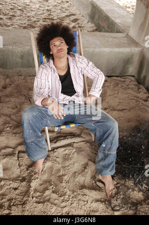 Junger Mann mit Afro-Frisur in einem Liegestuhl am Strand Stockfoto