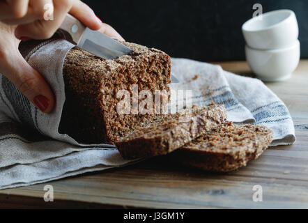 Das Mädchen schneidet Vollkornbrot Roggen auf einem Holztisch. Stockfoto