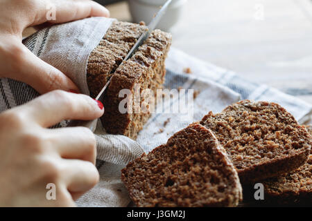 Das Mädchen schneidet Vollkornbrot Roggen auf einem Holztisch. Stockfoto