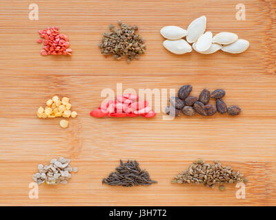 Verschiedene Samen auf Holzbrett Hintergrund gesetzt. Acht kleine getrennte Stapel. Tomaten, Karotten, Zucchini, Paprika, Gurke, Wassermelone, Kirsche toma Stockfoto