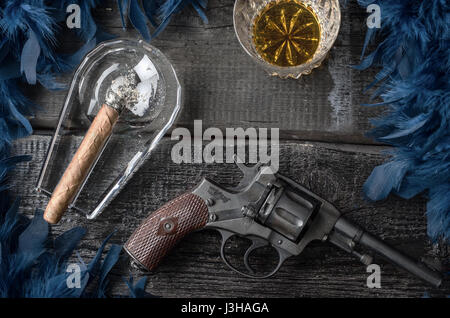 Thompson-Pistole, Revolver, Zigarren Aschenbecher, Whiskeyglas und blaue Federboa Stockfoto