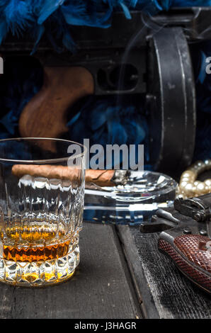 Thompson-Pistole, Revolver, Zigarren Aschenbecher, Whiskeyglas und blaue Federboa Stockfoto