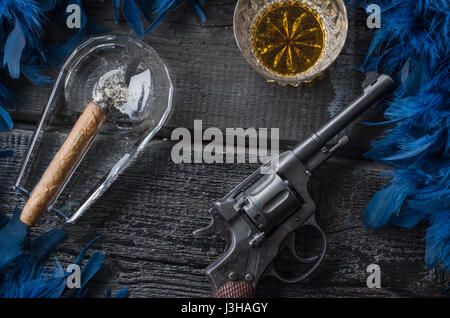 Thompson-Pistole, Revolver, Zigarren Aschenbecher, Whiskeyglas und blaue Federboa Stockfoto